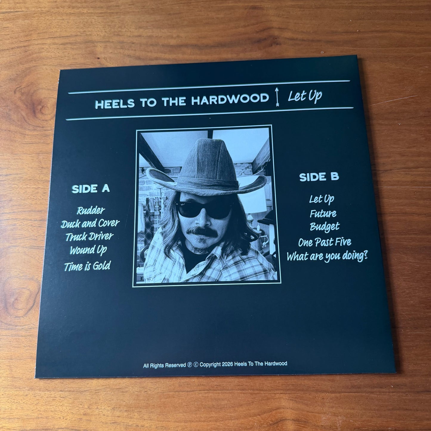 Vinyl record cover with text and black and white image on a wooden surface